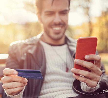 Man holding up debit card and looking at his mobile device
